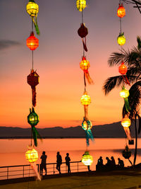 Illuminated lanterns hanging over sea against sky during sunset