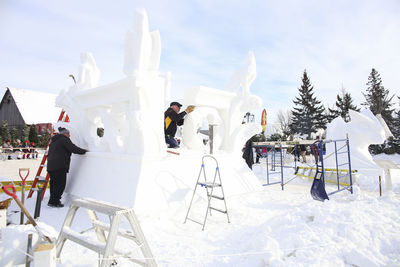 People on snow covered field against sky