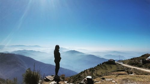 Man standing on rock against blue sky