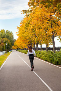 Rear view of woman on road amidst trees during autumn