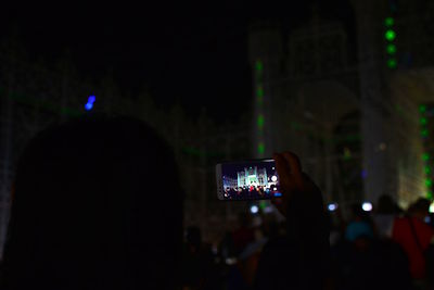 Rear view of person photographing illuminated smart phone at night