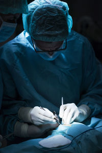 Man in surgeon uniform and his assistant performing surgery in dark operating theater