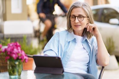 Mature european woman seated at an outdoor cafe, browsing information on her tablet pc. 