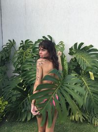 Portrait of young woman standing by plants against wall