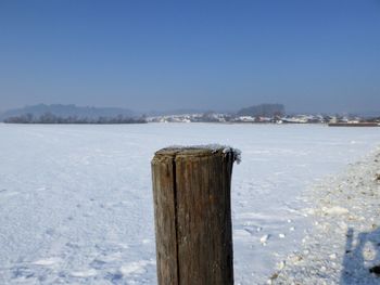 Wooden posts on frozen lake against clear sky