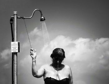 Woman taking shower against sky