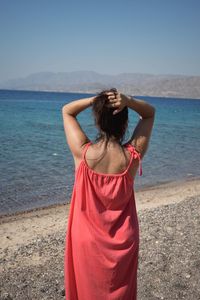 Rear view of woman standing at beach against clear sky