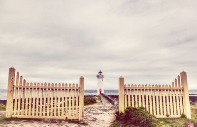 Lighthouse on shore against cloudy sky