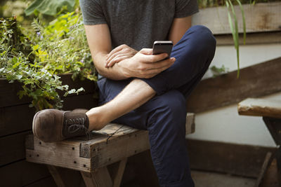 Low section of man using smart phone while sitting on bench