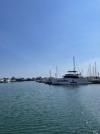 Sailboats moored in sea against clear blue sky