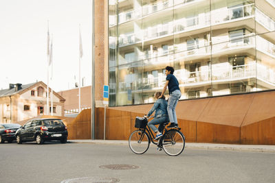 Side view of young man riding bicycle with friend on street in city