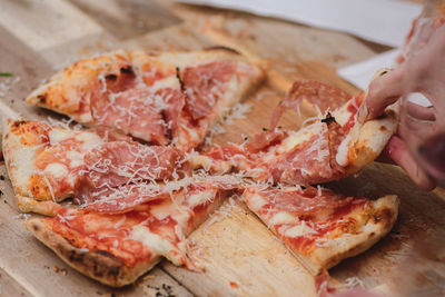 Hands taking pieces or slices of pizza with tomato sauce, mozzarella, parmesan cheese and salami