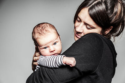 Side view of mother carrying cute son while standing against gray background