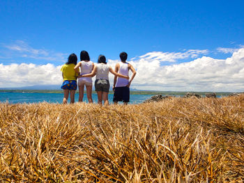 Rear view of friends standing at beach against sky