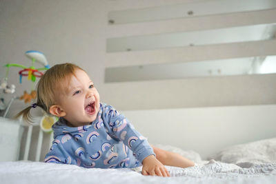 Cute baby girl with mouth open relaxing on bed at home