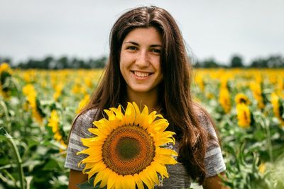 Portrait of smiling woman holding sunflower against flowering plants