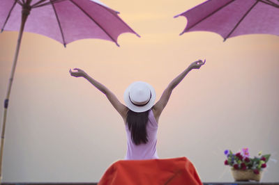 Rear view of woman with arms raised standing against sky