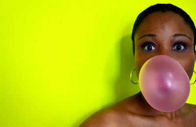 Portrait of woman blowing bubble against yellow background