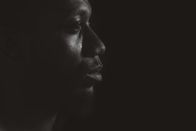 Close-up of man looking away and crying against black background