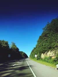 Road amidst trees against clear blue sky