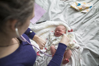 High angle view of midwife examining newborn baby girl with stethoscope on bed at home