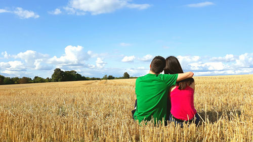 Rear view of couple sitting on field against sky