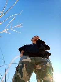 Low angle view of man standing against clear blue sky