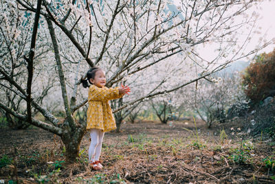 Full length of a girl holding tree in forest