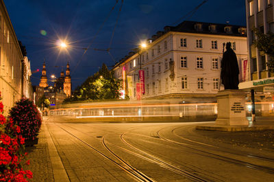 Light trails on road by buildings against sky in city at night