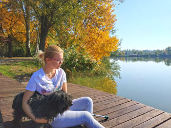 Young woman with black hairy dog sitting on pier by lake