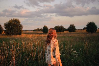 Woman standing on field against sky during sunset