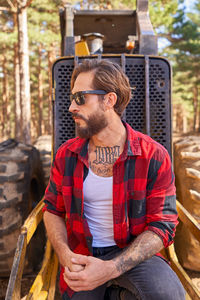 Portrait of young tattoed man leaning on against an excavator
