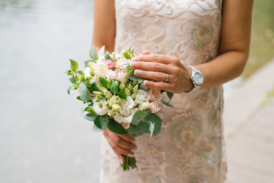 Bride in a beige wedding dress holds a bouquet of flowers and greenery in her hands