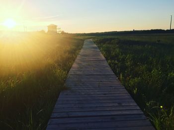 Boardwalk on field against sky during sunset