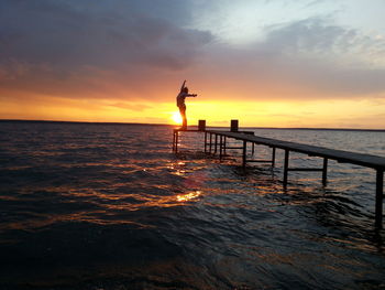 Silhouette people on pier at sunset