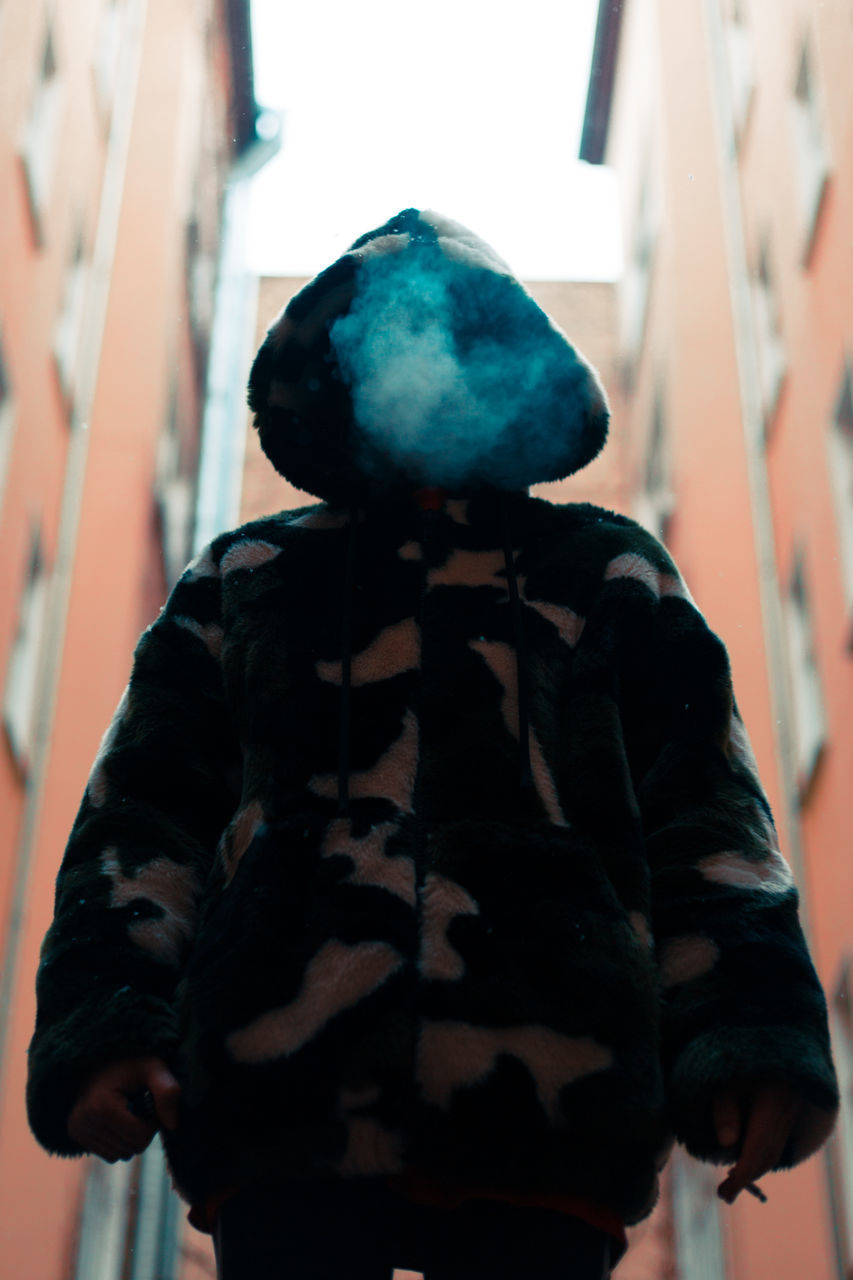 REAR VIEW OF WOMAN STANDING AGAINST WALL