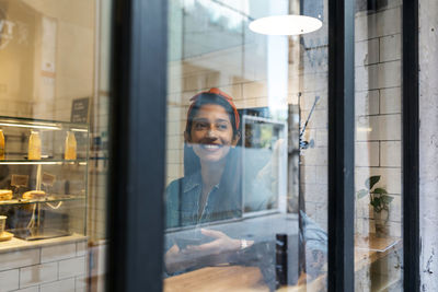 Portrait of smiling woman seen through glass window