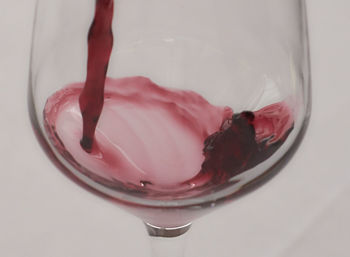 Close-up of red wine pouring in glass against white background