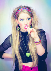 Portrait of young woman eating lollipop against wall