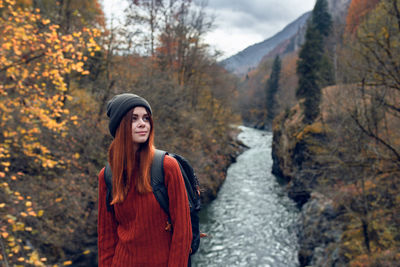 Young woman looking away while standing by trees during autumn