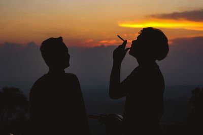 Silhouette man smoking cigarette against sky during sunset