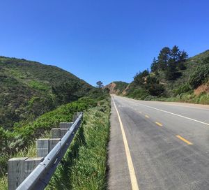 Road amidst trees against clear blue sky