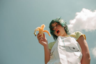 Low angle view of woman having banana against sky