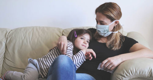 Sick mother with surgical mask stay with her child on the sofa .