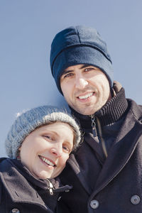 Portrait of smiling mid adult couple standing against wall during winter