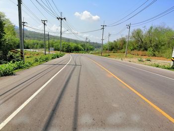 Road by electricity pylon against sky