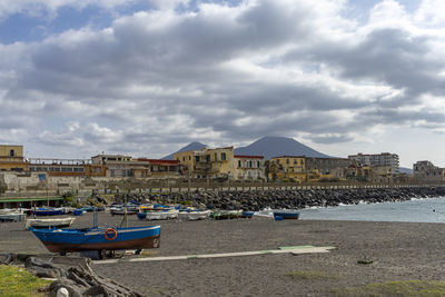 Boats moored on beach by buildings against sky in city