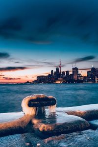 Sea by modern buildings against sky at sunset