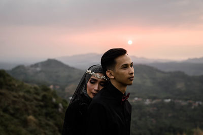 Young man standing on mountain against sky during sunset