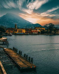 Scenic view of lake by buildings against sky during sunset